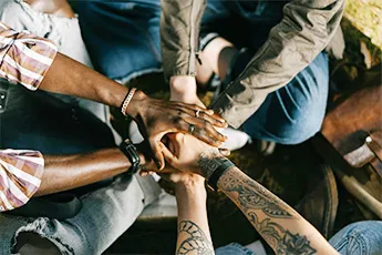 Building support networks icon featuring a group of people sitting in a circle with their hands stacked on top of each other in the center, symbolizing unity and mutual support