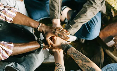 Building support networks icon featuring a group of people sitting in a circle with their hands stacked on top of each other in the center, symbolizing unity and mutual support