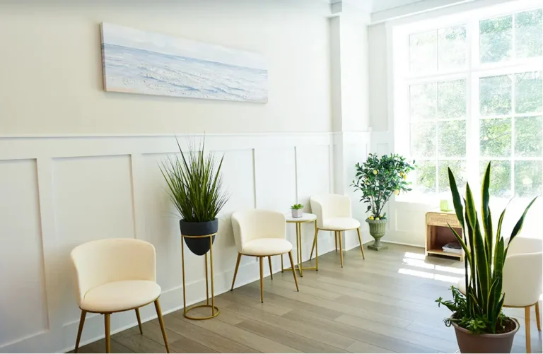 Bright and modern waiting area at South Carolina Turnwell location featuring white chairs, green plants, large windows, and a beach landscape painting.