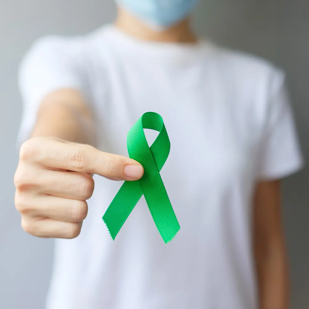 A person holds a green awareness ribbon, a universal symbol of mental health advocacy and support.