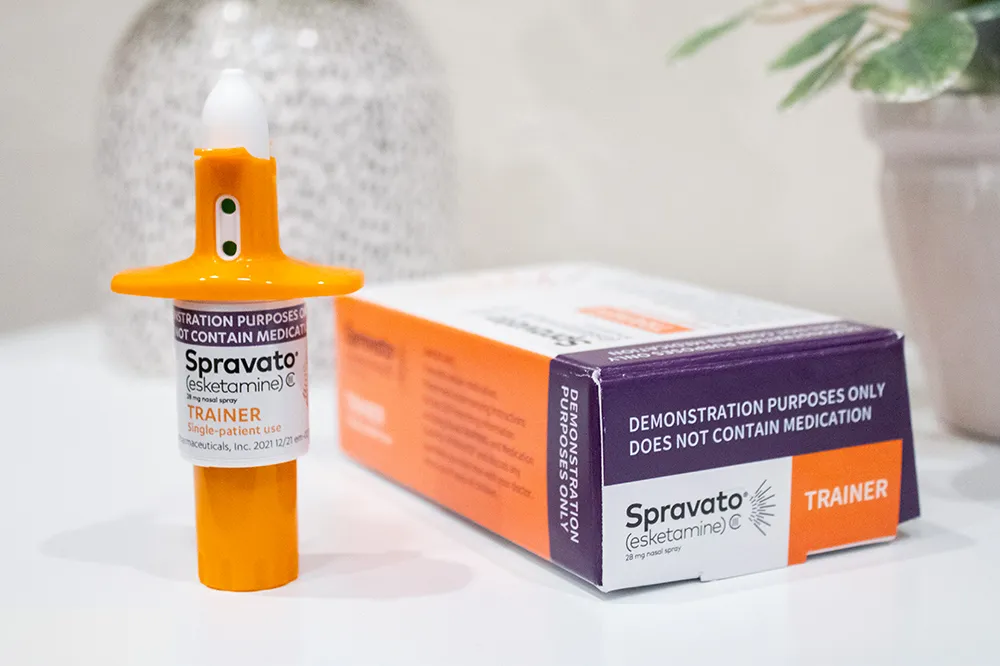 A bottle of Spravato (esketamine) nasal spray is placed on a counter. The setting is clean and clinical, emphasizing the importance of proper medication storage and accessibility.